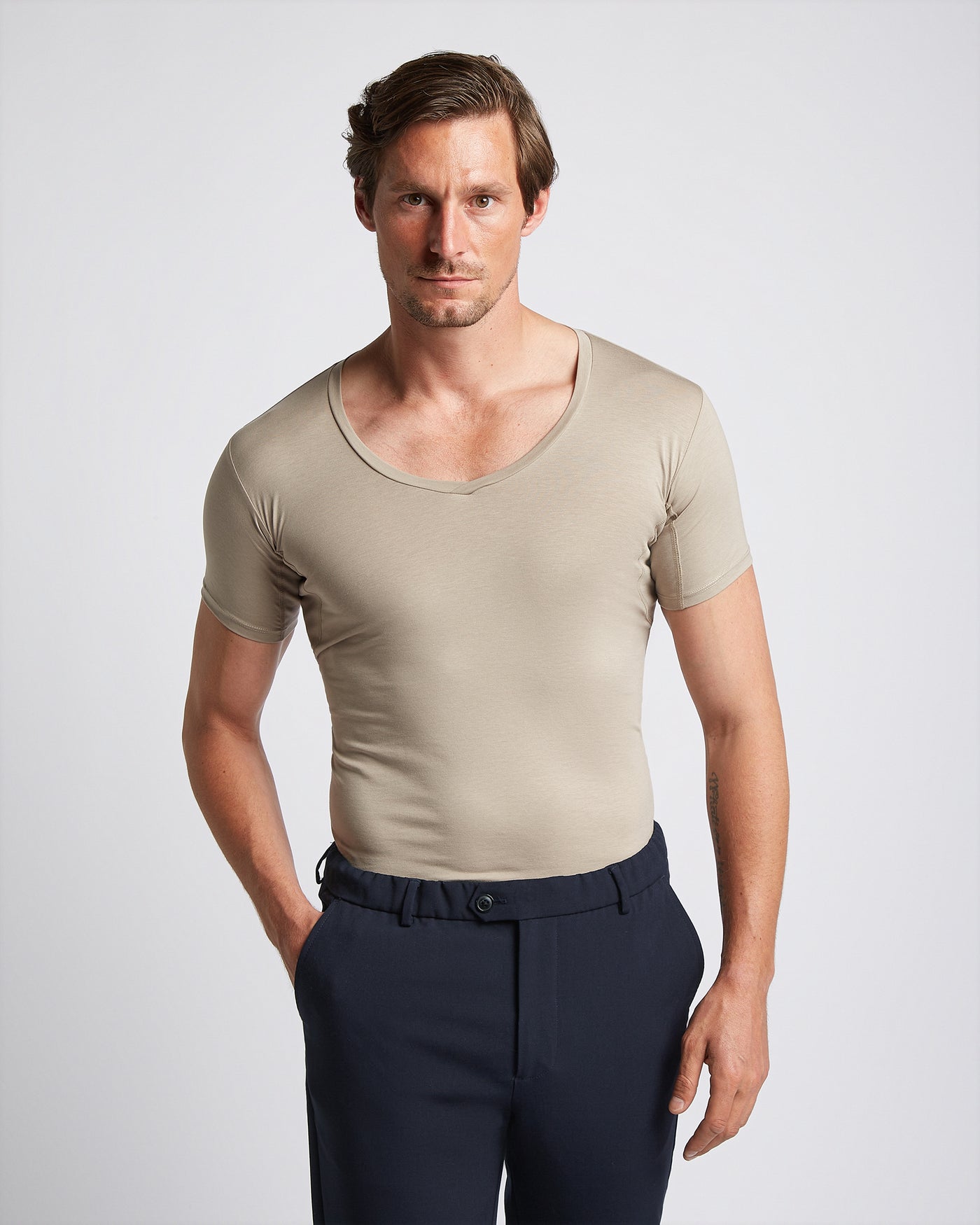 A man wearing a khaki-colored V-neck undershirt with short sleeves, paired with dark trousers.